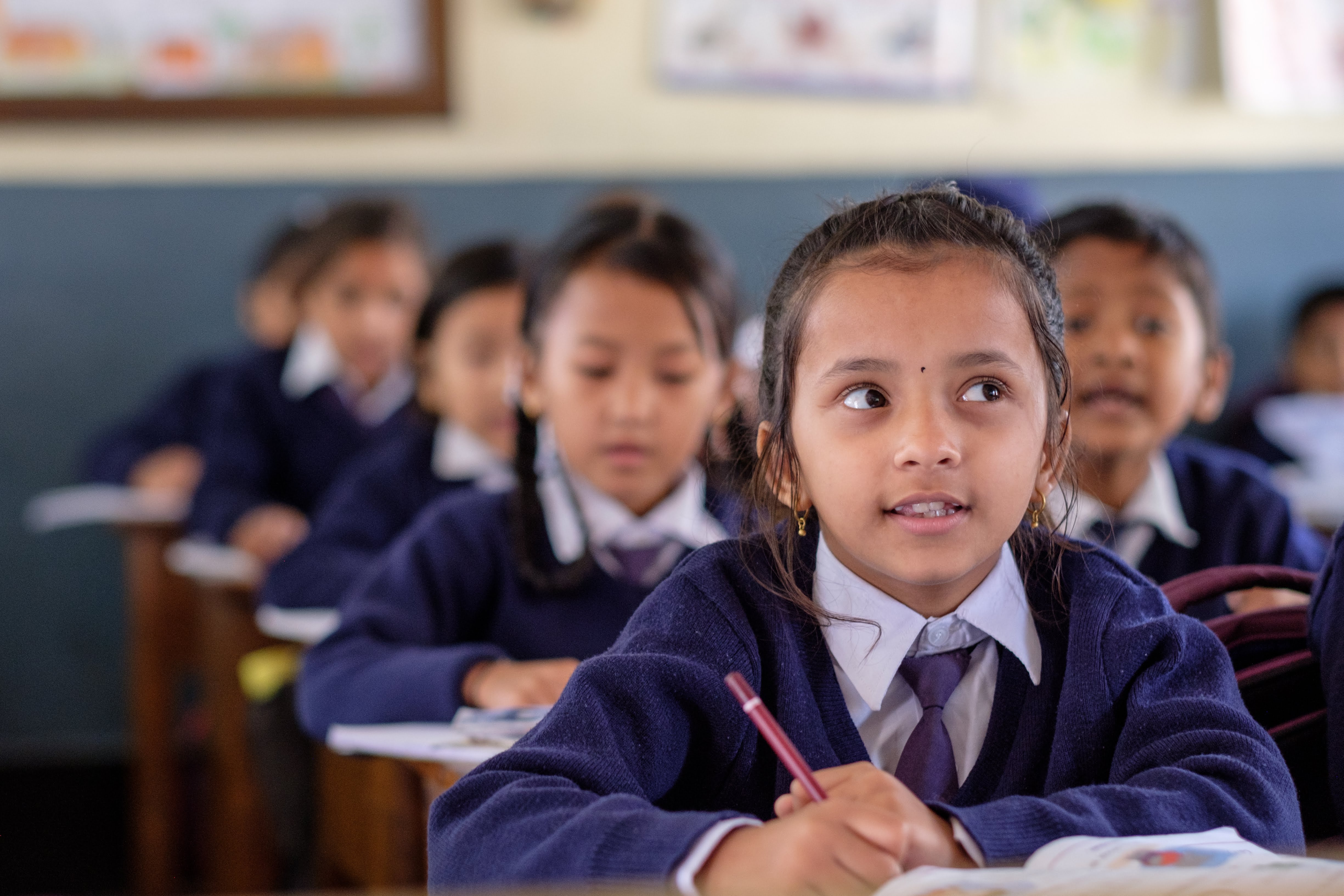 Young girl in school uniform attentively listening in a classroom.